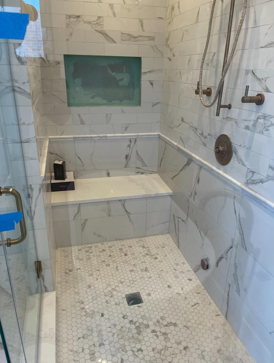 Calacatta marble walk-in shower with built-in bench and decorative niche — bronze fixtures, mosaic floor