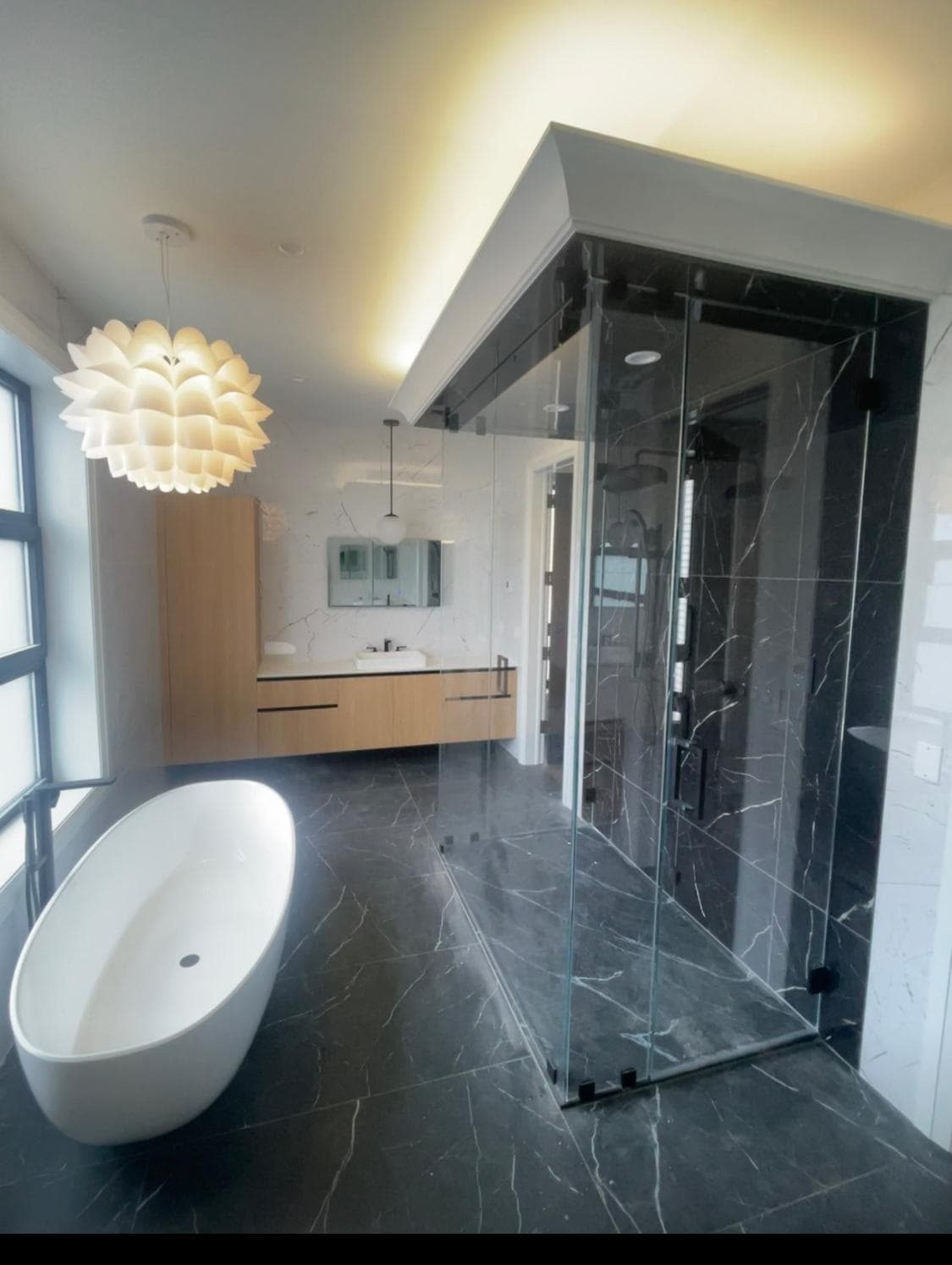 Dark marble spa bathroom with deep soaking tub and floor-to-ceiling stone — Epic Homes custom build